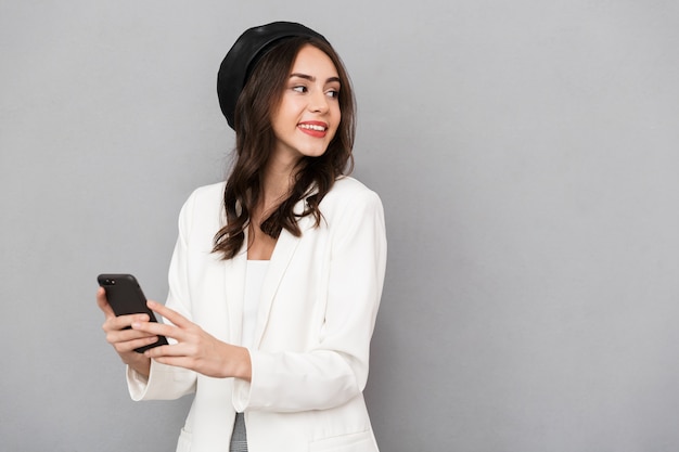 Portrait of a beautiful young woman dressed in jacket over gray background, using mobile phone