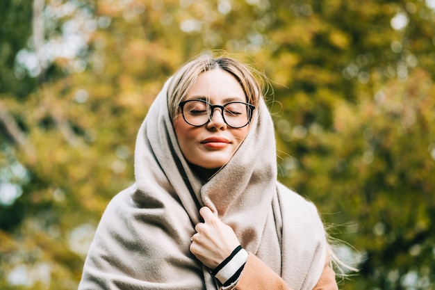 Portrait of beautiful young woman in eyeglasses, enjoying autumn weather in the park. Woman walking in the autumn park.