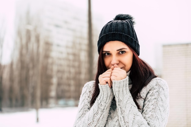 Portrait of a beautiful young woman in a gray knitted sweater standing outdoors during winter