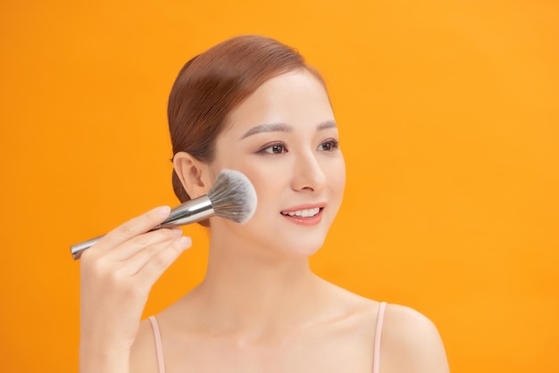 Portrait of a beautiful young woman holding a brush in her hand and applying powder to her face with a brush