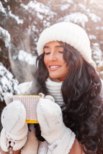 portrait of beautiful young woman holding mug with hot drink in the forest in winter