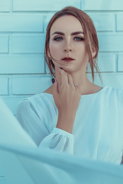 Portrait of a beautiful young woman in a long white dress, against white brick wall