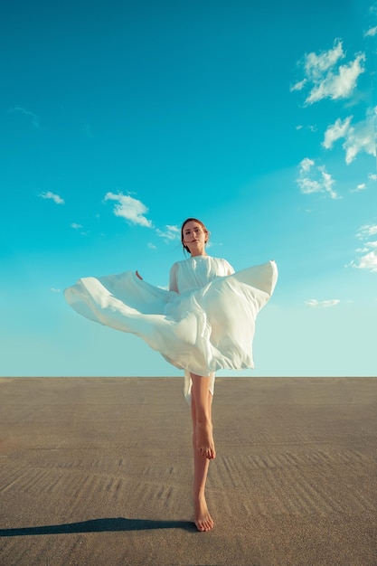 Portrait of beautiful young woman in long white dress standing on rooftop of building with cityscape