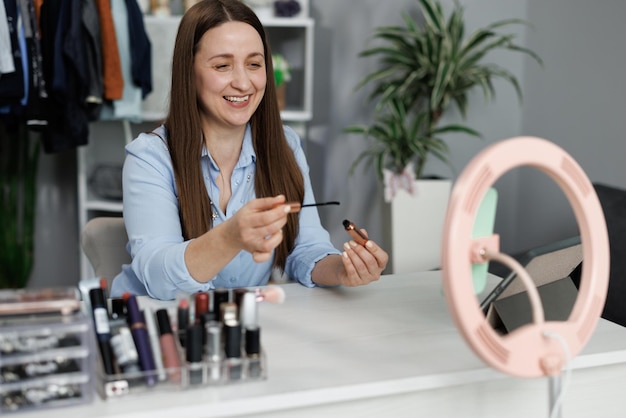 Portrait of beautiful young woman making makeup looking in the mirror and applying cosmetic cosmetic