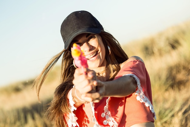 Portrait of beautiful young woman playing with water gun on field.