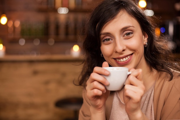 Portrait of beautiful young woman relaxing with a good coffee and smiling at camera in a coffee shop. Attractive woman having an aromatic coffee.