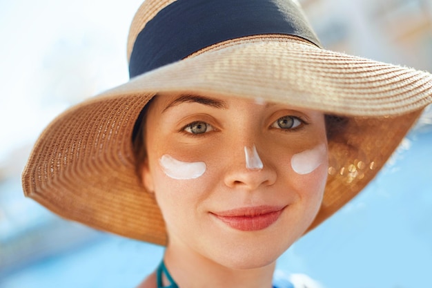 Portrait of a beautiful young woman smiling in a swimsuit smeared face with sun protection cream hat