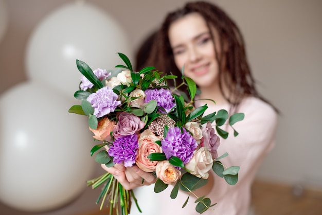 portrait of a beautiful young woman in a summer dress and a straw hat holds a carnation, roses bouquet and looking over her shoulder