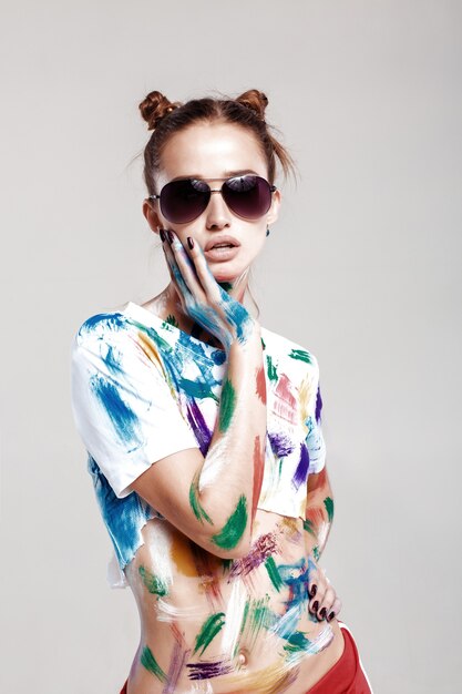 Portrait of beautiful young woman in sunglasses is dirty in multicolored paint.