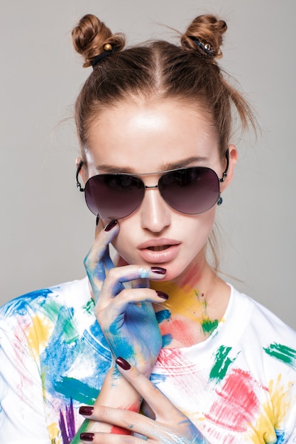 Portrait of beautiful young woman in sunglasses is dirty in multicolored paint.