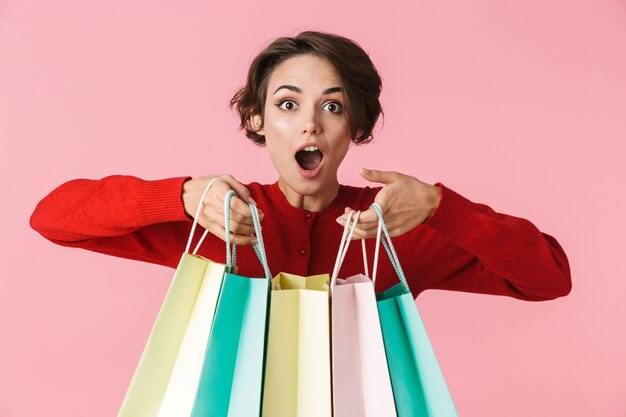 Portrait of a beautiful young woman wearing red clothes standing isolated, carrying shopping bags