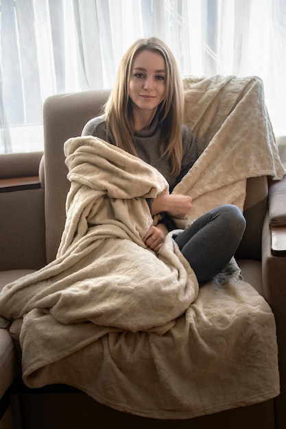 Portrait of a beautiful young woman who is cold at home and wraps herself in a blanket