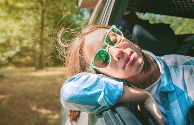 Portrait of beautiful young woman with her head over a open window car during a travel. Relax and nature concept.