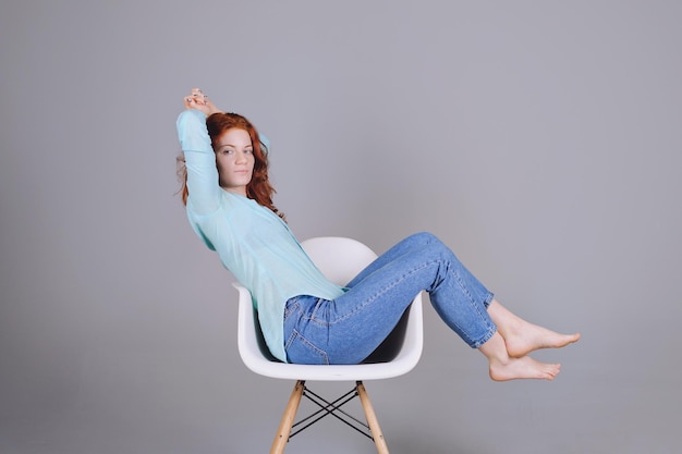 portrait of beautiful young woman with red curly hair and blue eyes against gray background.