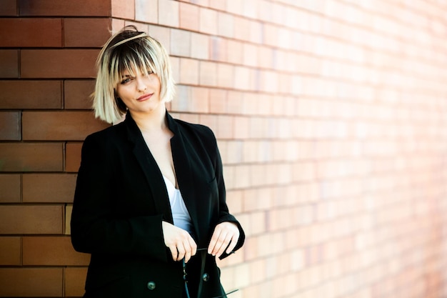 Portrait of a beautiful young woman with short hair in a black coat against a brick wall