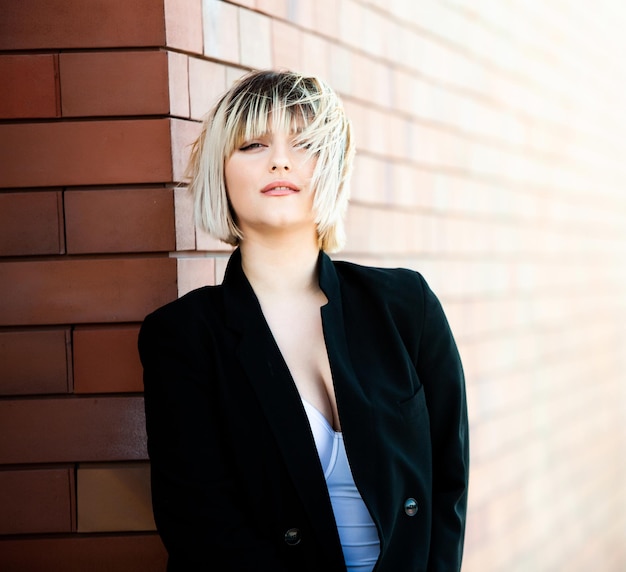 Portrait of a beautiful young woman with short hair in a black coat against a brick wall