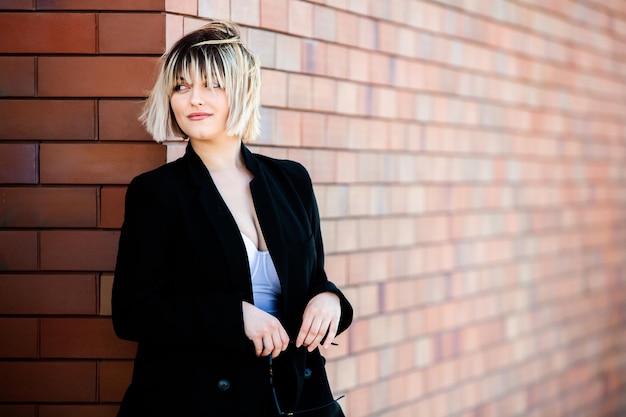 Portrait of a beautiful young woman with short hair in a black coat against a brick wall