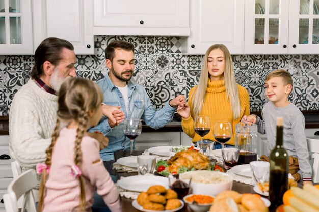 Portrait of big family sitting at festive table and holding each other by hands while praying