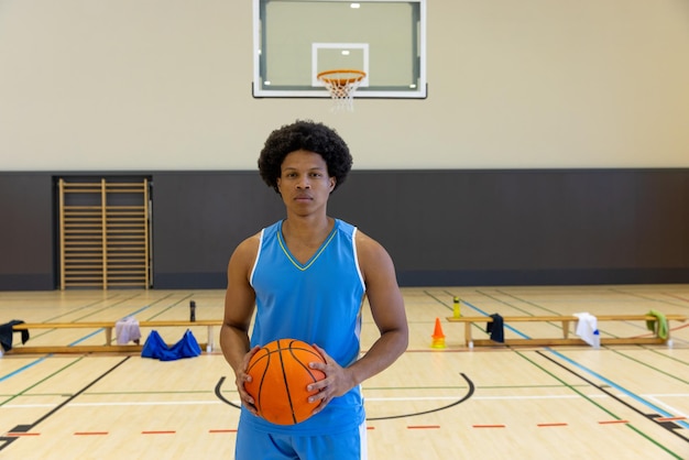 Portrait of biracial male basketball player with basketball wearing blue sports clothes at gym. Sport, activity and lifestyle, unaltered.