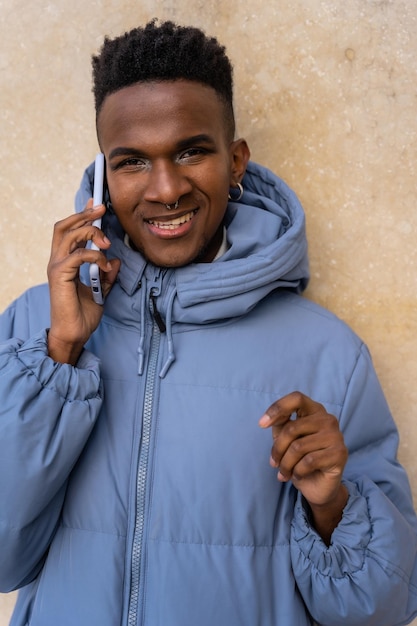 Portrait of a black ethnic man with a phone and a blue jacket on a yellow background talking on the phone