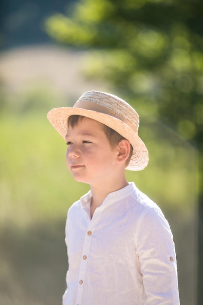 Portrait of the blode hair boy in straw hat with blurred summer greenery background