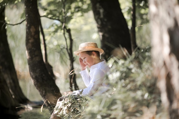 Portrait of the blode hair boy in straw hat with blurred summer greenery background