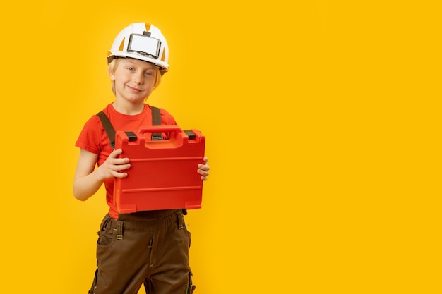 Portrait of blond boy in white protective helmet with box for instruments is insulated on yellow background Copy space mockup