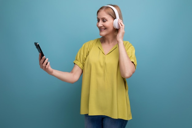 Portrait of a blond mature aged woman with a gadget to listen to songs on a studio background with