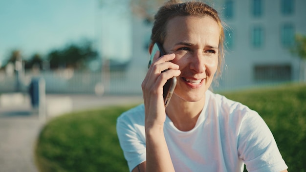 Portrait of blond woman looking happy talking over smartphone while waiting beginning of workout in city park