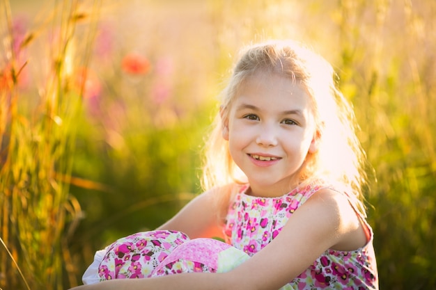 The portrait of blonde girl seating in the blossom field n the sunset.