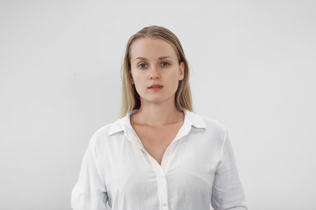 Portrait of blonde girl in white shirt on white wall,