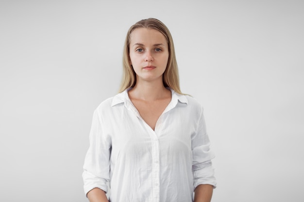 Portrait of blonde girl in white shirt on white wall,