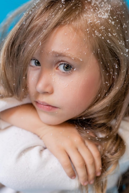 portrait of a blonde girl in a winter knitted hat. artificial snow in the studio