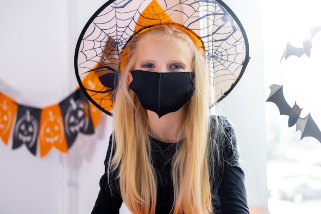 Portrait blonde girl in witch costume wearing face masks preparing for Halloween protecting from COVID19