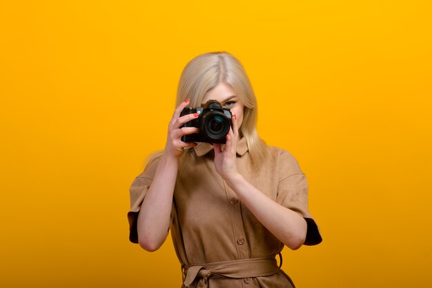 Portrait of a blonde girl with a camera in hand on yellow