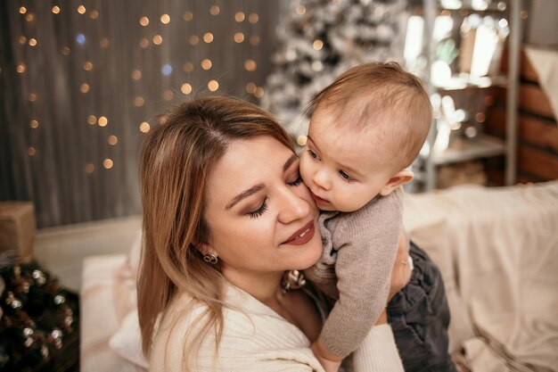 Portrait of a blonde mom holding a baby baby on the background of a Christmas tree