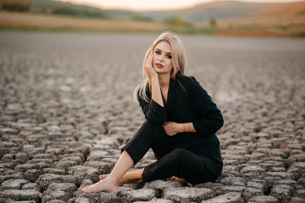 the portrait of a blonde sitting on a dry lake