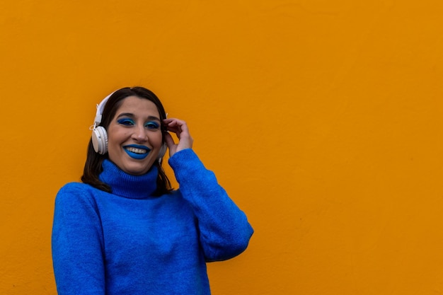 Portrait of a blue make up woman with headphones smiling on a yellow background