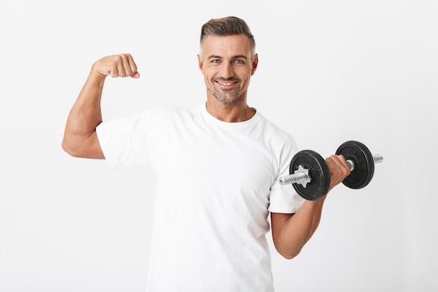 Portrait of bodybuilder man 30s with bristle wearing casual t-shirt pumping biceps and lifting dumbbell isolated on white