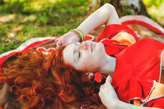 Portrait of boho young woman in summer countryside. Red curly hair, blue eyes. Happy lifestyle.