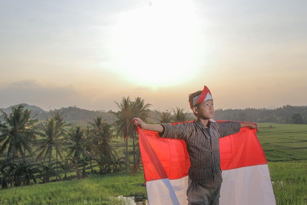 portrait of a boy carrying a red and white flag and spreading his hands in the fields