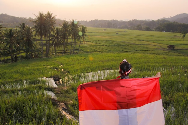 portrait of a boy carrying a red and white flag with a view of rice fields.