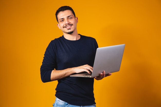 Portrait of boy holding laptop working in hands isolated over yellow background.