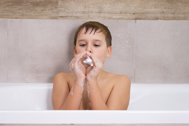 Portrait of boy playing with with soap shampoo or gel in bathroom child bathe and inflates soap bubbles