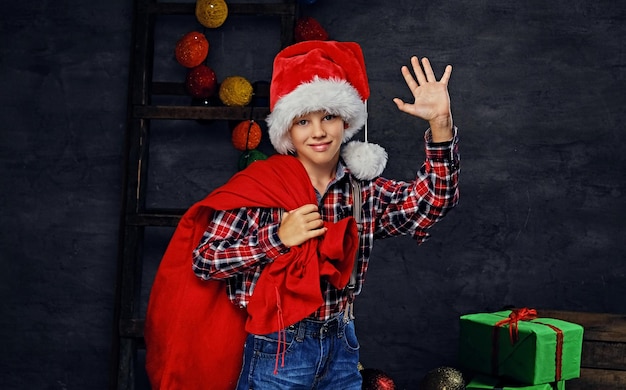 Photo portrait of a boy in santa's costume with red bag on a shoulder.