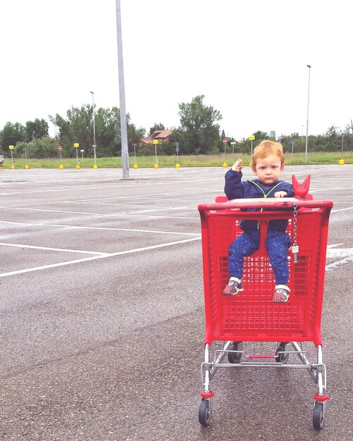 Photo portrait of boy sitting on shopping cart against sky