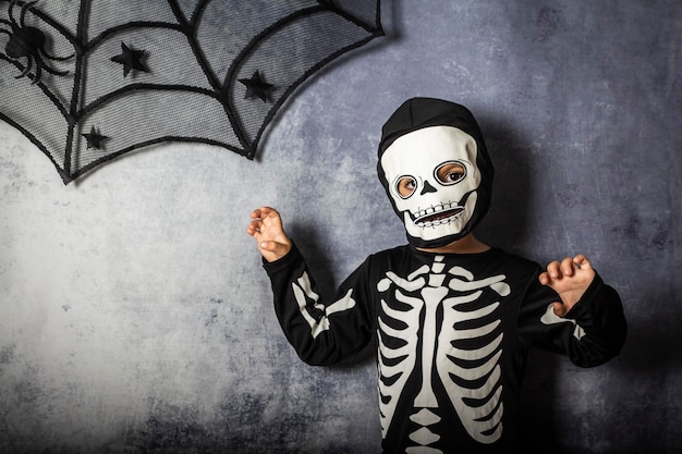 Photo portrait of boy in skeleton costume making scary gesture against gray wall