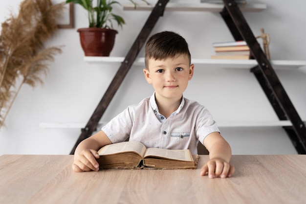 Portrait of a boy student sitting at a desk studying online listening to the teacher Schoolboy doing homework sitting with an open textbook or book Home education concept