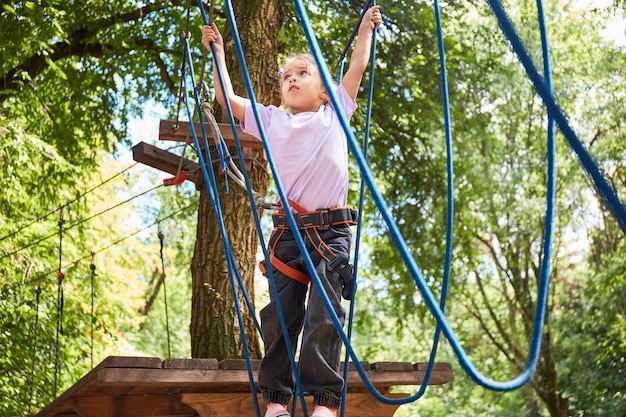 Portrait of brave little girl walk on a rope bridge in an adventure rope park Having fun at adventure park Scout practicing rappelling