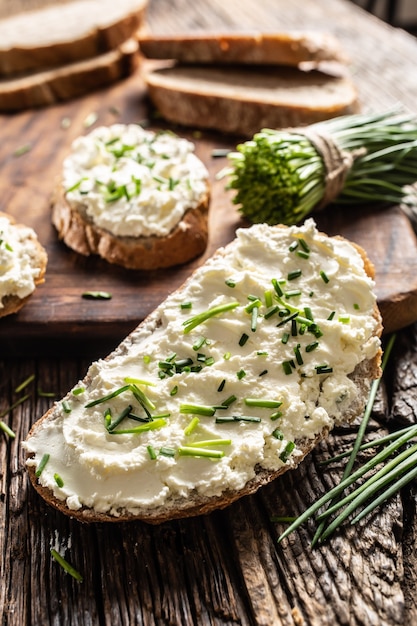 Portrait of bread slice with traditional Slovak bryndza cream cheese spread with freshly cut chives placed on rustic wood.